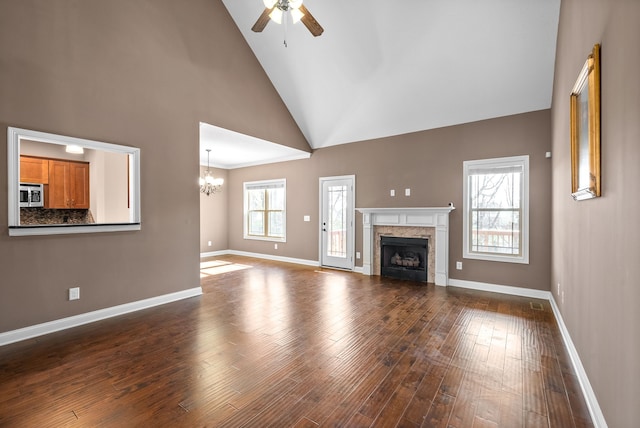 unfurnished living room with ceiling fan with notable chandelier, high vaulted ceiling, and dark hardwood / wood-style floors