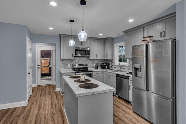 kitchen with gray cabinetry, wood-type flooring, decorative light fixtures, and appliances with stainless steel finishes