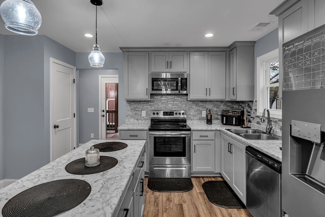 kitchen with decorative backsplash, appliances with stainless steel finishes, sink, decorative light fixtures, and light hardwood / wood-style floors