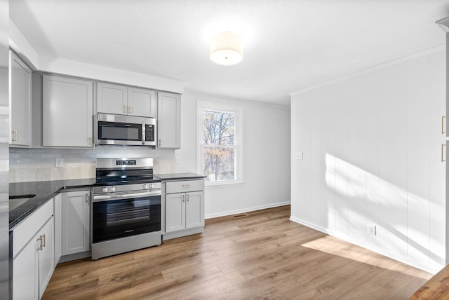 kitchen featuring light wood-type flooring, tasteful backsplash, ornamental molding, stainless steel appliances, and gray cabinets