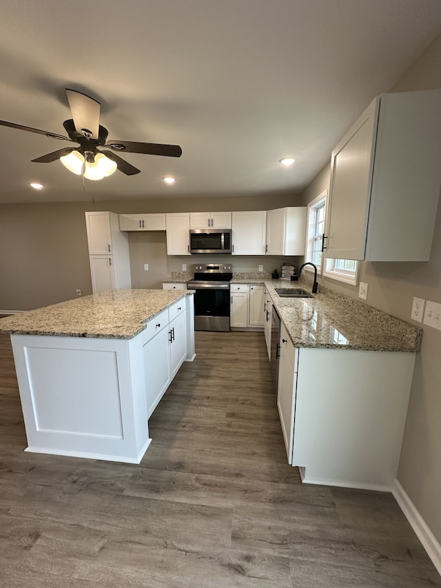 kitchen with white cabinetry, sink, light stone countertops, a kitchen island, and appliances with stainless steel finishes