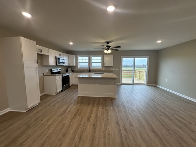 kitchen with hardwood / wood-style floors, a center island, ceiling fan, appliances with stainless steel finishes, and white cabinetry