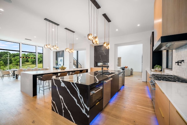 kitchen featuring light stone countertops, sink, a large island with sink, decorative light fixtures, and light wood-type flooring