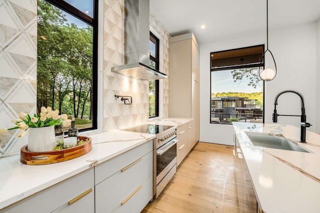 kitchen featuring stainless steel electric range oven, white cabinets, pendant lighting, and wall chimney range hood