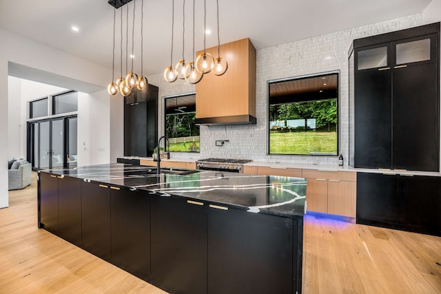 kitchen with a wealth of natural light, a center island with sink, hanging light fixtures, and light wood-type flooring