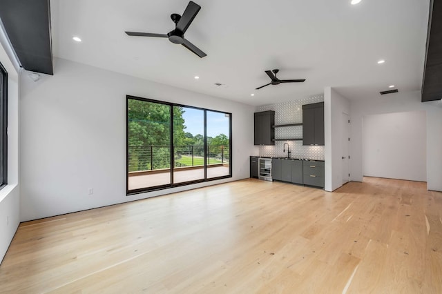 unfurnished living room with ceiling fan, sink, beverage cooler, and light hardwood / wood-style flooring