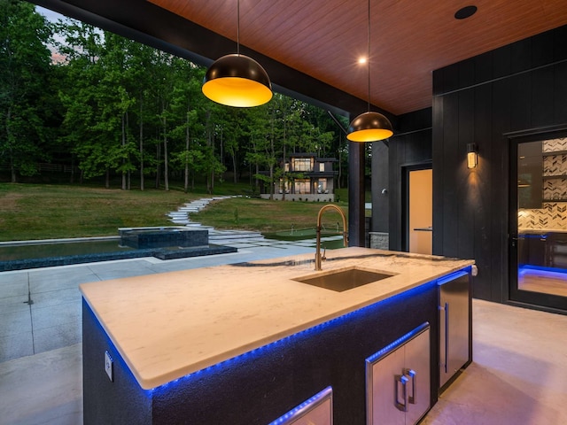 exterior space with a center island with sink, hanging light fixtures, wood walls, and sink