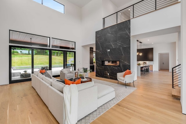 living room featuring light wood-type flooring, a towering ceiling, and a premium fireplace