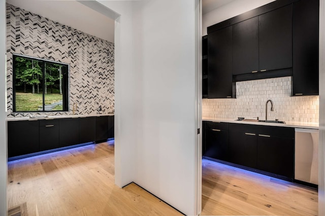 kitchen with stainless steel dishwasher, backsplash, light hardwood / wood-style floors, and sink