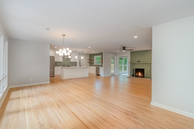 unfurnished living room featuring ceiling fan with notable chandelier, a brick fireplace, and light hardwood / wood-style flooring