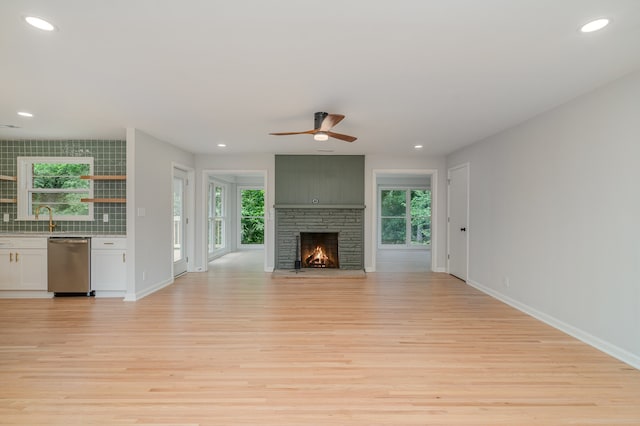 unfurnished living room featuring a large fireplace, sink, ceiling fan, and light hardwood / wood-style flooring