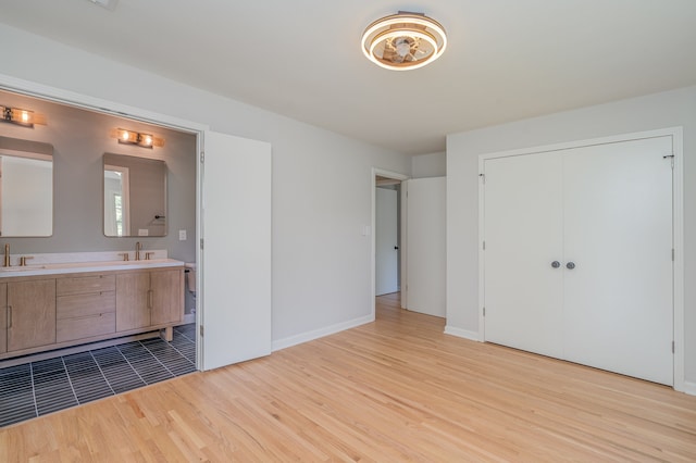 unfurnished bedroom with ensuite bath, sink, a closet, and light wood-type flooring