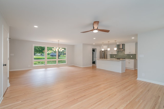 unfurnished living room with ceiling fan with notable chandelier and light hardwood / wood-style flooring