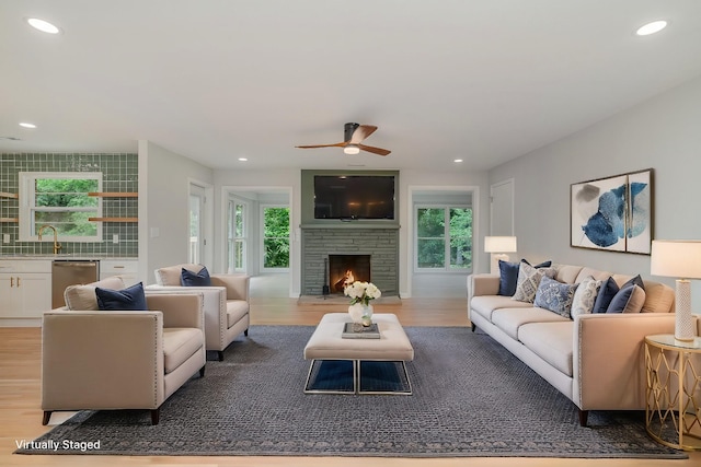 living room with ceiling fan, a stone fireplace, sink, and light wood-type flooring