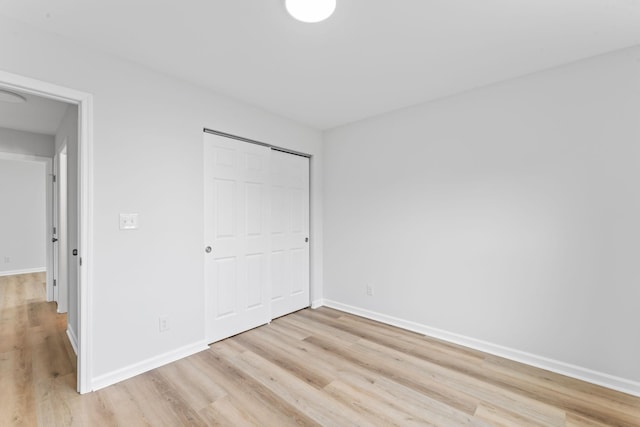 unfurnished bedroom with light wood-style floors, a closet, and baseboards