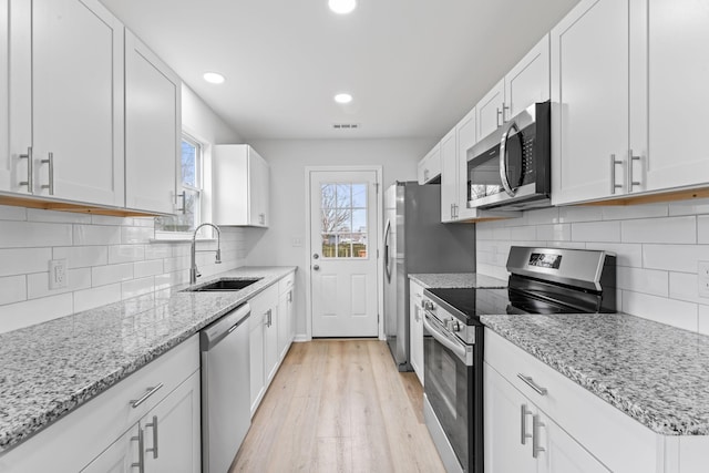 kitchen featuring appliances with stainless steel finishes, a sink, light wood-style flooring, and white cabinets