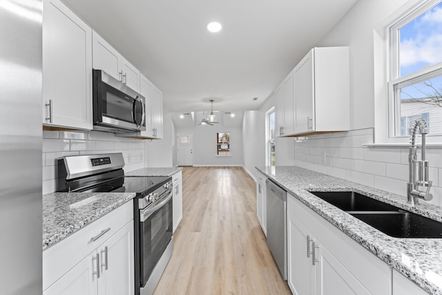 kitchen with light wood-style flooring, decorative backsplash, appliances with stainless steel finishes, white cabinets, and a sink