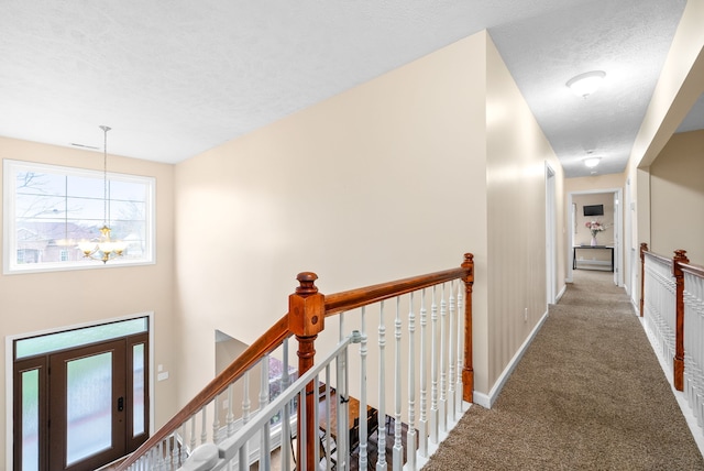 hall with carpet floors, a textured ceiling, and an inviting chandelier