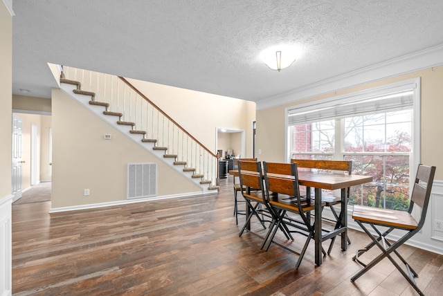 dining space with a textured ceiling, ornamental molding, and dark wood-type flooring