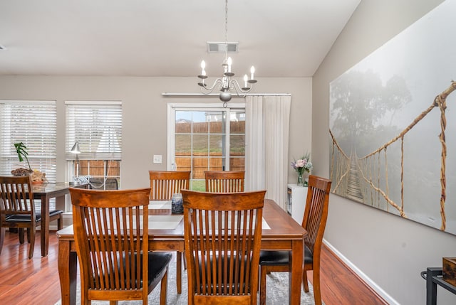 dining space featuring vaulted ceiling, wood-type flooring, and an inviting chandelier