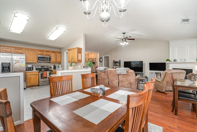 dining space featuring ceiling fan with notable chandelier, light hardwood / wood-style flooring, vaulted ceiling, and a large fireplace