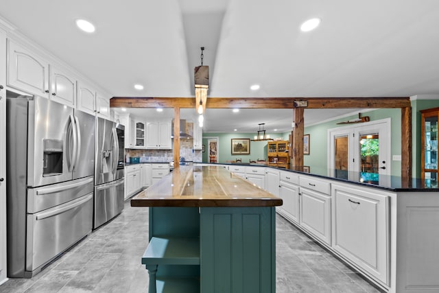 kitchen featuring decorative light fixtures, stainless steel fridge, kitchen peninsula, and white cabinets