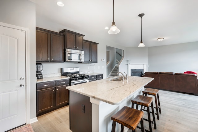 kitchen featuring appliances with stainless steel finishes, light wood-type flooring, a breakfast bar, pendant lighting, and an island with sink