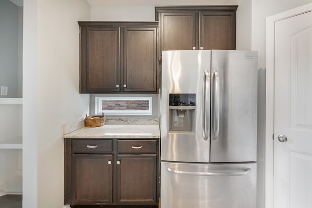 kitchen with stainless steel fridge, light stone counters, and dark brown cabinets