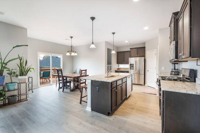 kitchen featuring light stone countertops, stainless steel appliances, pendant lighting, light hardwood / wood-style floors, and a kitchen island with sink