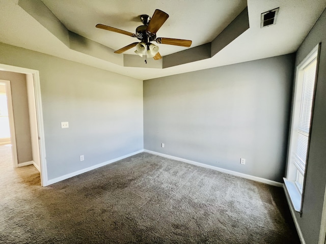 carpeted spare room featuring a tray ceiling and ceiling fan