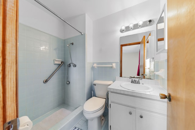 bathroom with tile patterned floors, toilet, tiled shower, vanity, and tile walls