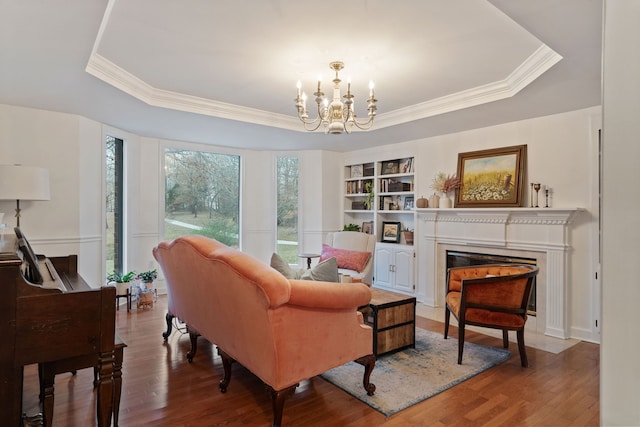 living area with a tray ceiling, built in features, a notable chandelier, and hardwood / wood-style flooring