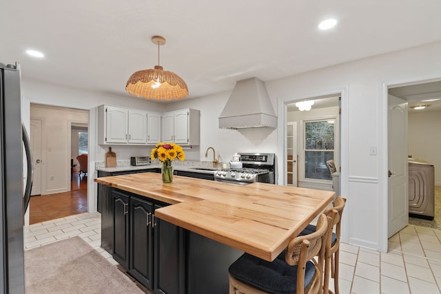 kitchen with sink, hanging light fixtures, stainless steel appliances, wooden counters, and custom range hood