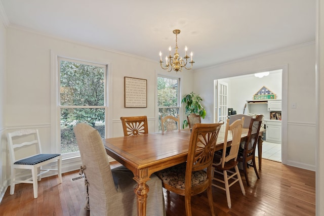 dining area with wood-type flooring, an inviting chandelier, and crown molding