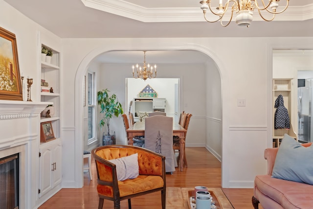 living room featuring a chandelier, light hardwood / wood-style floors, built in features, and crown molding