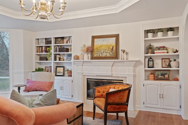 living area with an inviting chandelier, built in features, crown molding, a fireplace, and light wood-type flooring