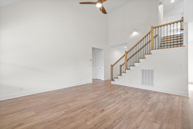 unfurnished living room featuring a towering ceiling, light hardwood / wood-style flooring, and ceiling fan