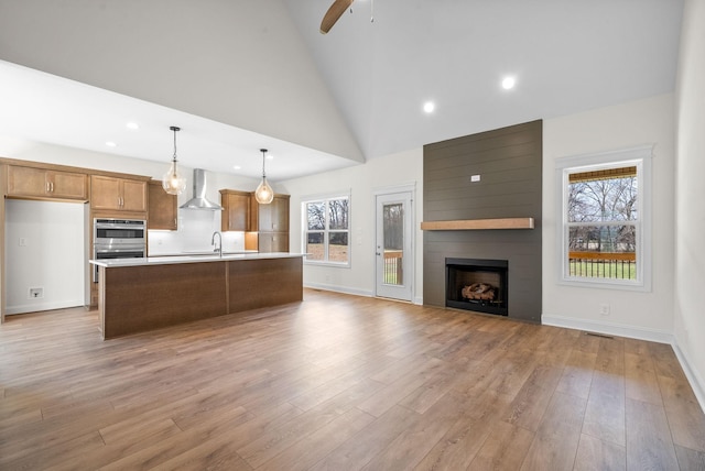 kitchen with pendant lighting, high vaulted ceiling, wall chimney exhaust hood, a fireplace, and an island with sink