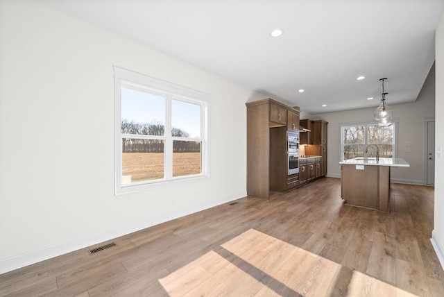 kitchen featuring light wood-type flooring, a breakfast bar, sink, pendant lighting, and an island with sink