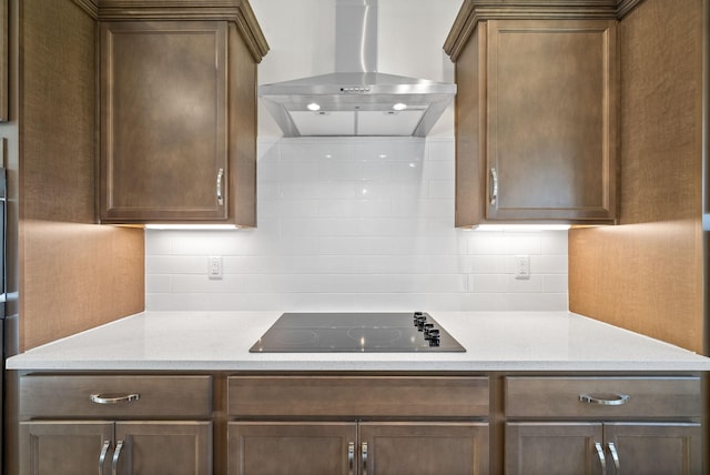 kitchen featuring black electric stovetop, wall chimney exhaust hood, light stone counters, and tasteful backsplash