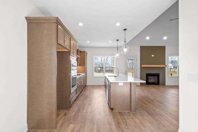 kitchen with a kitchen island with sink, sink, hanging light fixtures, light hardwood / wood-style flooring, and a large fireplace