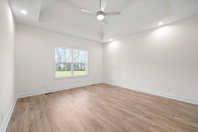 spare room with ceiling fan, a raised ceiling, and light hardwood / wood-style flooring