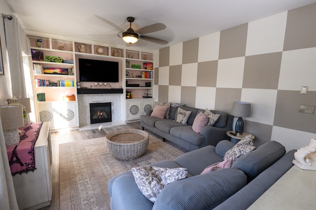 living room featuring a tile fireplace, built in shelves, light wood-type flooring, and ceiling fan