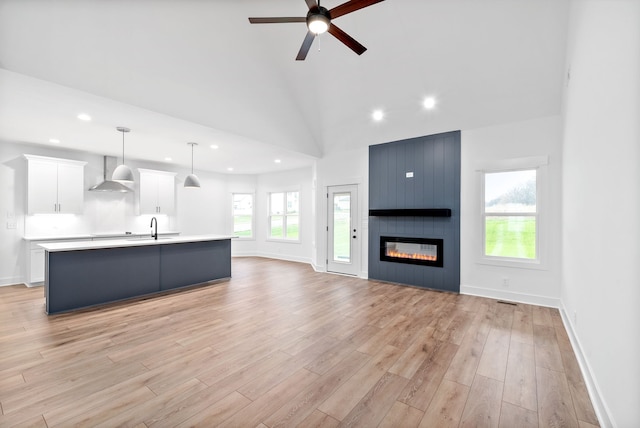 unfurnished living room with light wood-type flooring, a large fireplace, ceiling fan, sink, and high vaulted ceiling