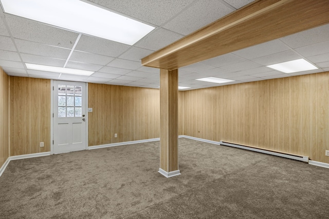 basement featuring wood walls, a drop ceiling, carpet, and a baseboard heating unit