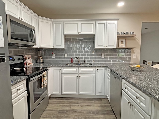 kitchen featuring white cabinetry, sink, stainless steel appliances, dark stone counters, and light wood-type flooring