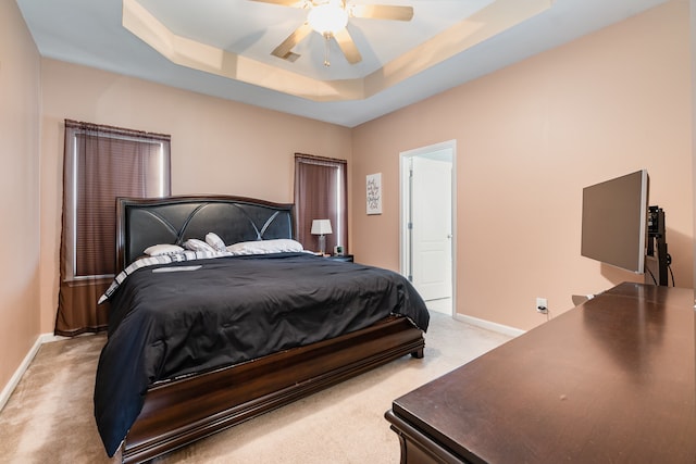 bedroom with light colored carpet, ceiling fan, and a tray ceiling