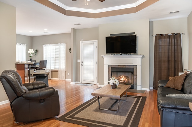 living room featuring hardwood / wood-style floors, a tile fireplace, a raised ceiling, crown molding, and ceiling fan