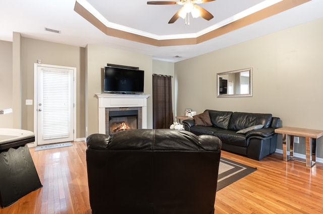 living room with crown molding, hardwood / wood-style flooring, ceiling fan, a tray ceiling, and a tiled fireplace