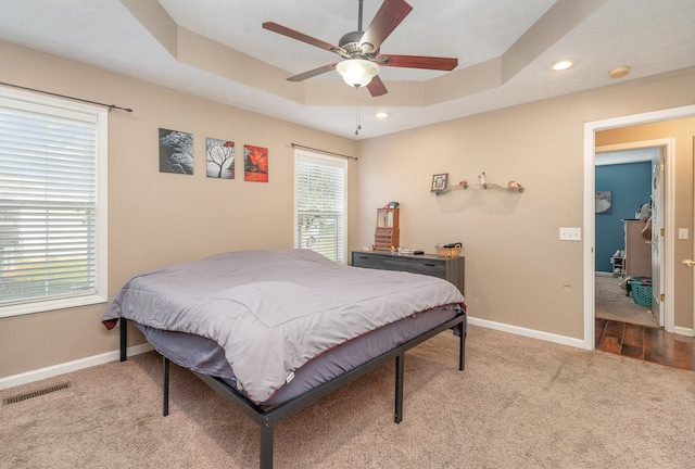 bedroom featuring ceiling fan, light colored carpet, a tray ceiling, and multiple windows